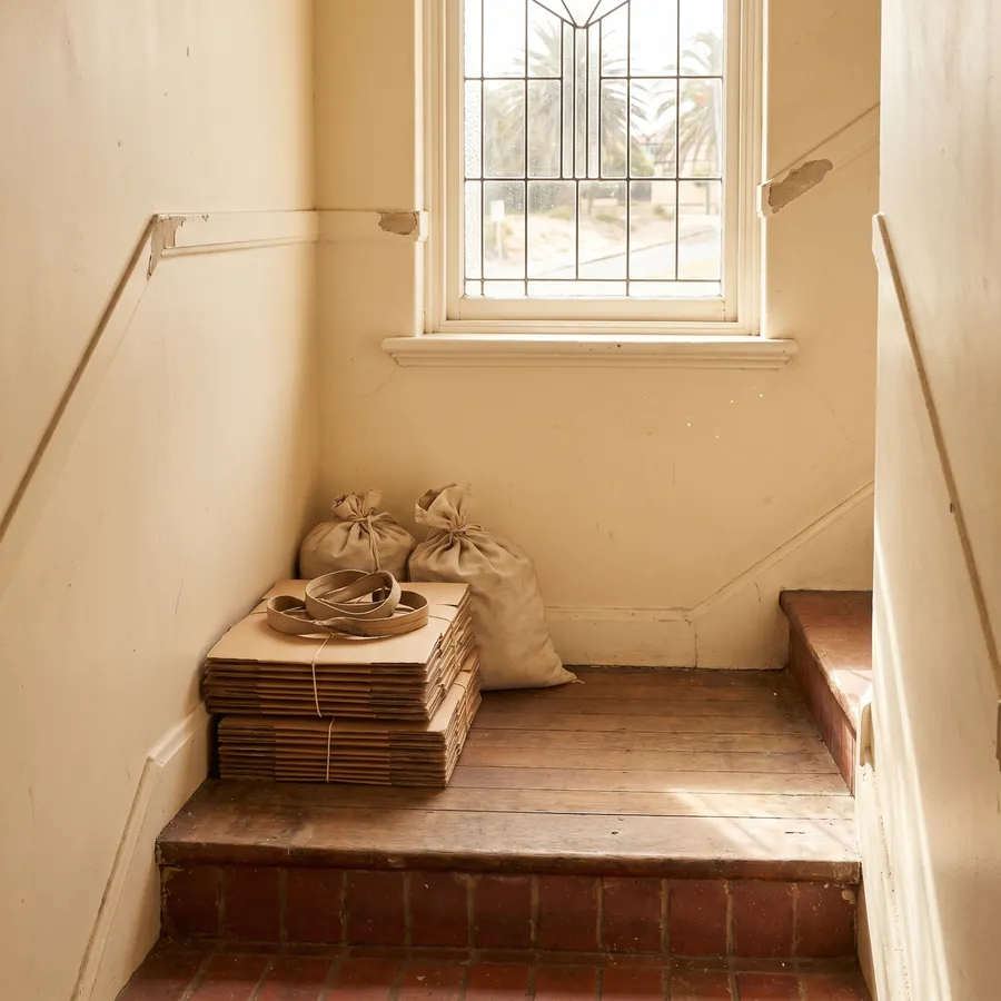 Flattened boxes and tied bags staged neatly on a walk-up half-landing with a carry strap coiled on top